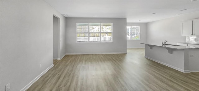 unfurnished living room with a sink, baseboards, and light wood finished floors