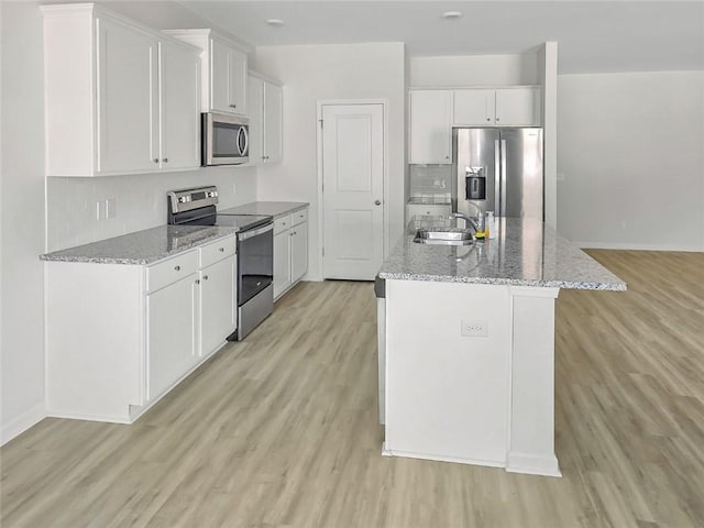 kitchen with a kitchen island with sink, a sink, stainless steel appliances, white cabinetry, and light wood-type flooring