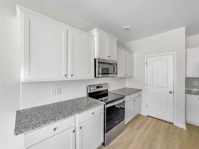 kitchen featuring light wood-type flooring, light stone counters, decorative backsplash, appliances with stainless steel finishes, and white cabinetry