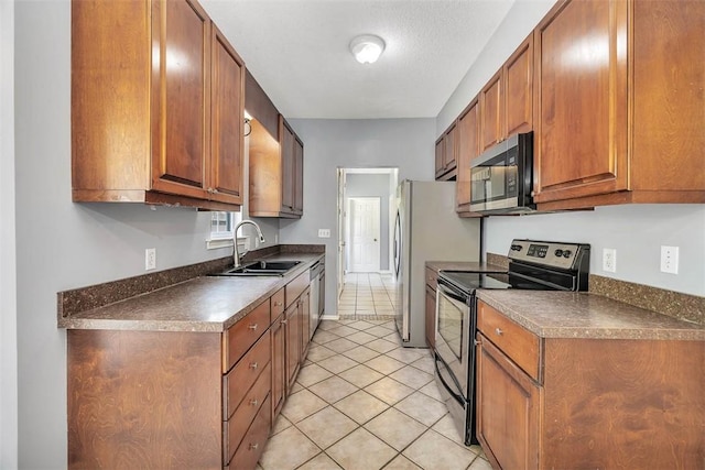 kitchen featuring light tile patterned floors, a sink, dark countertops, stainless steel appliances, and brown cabinetry