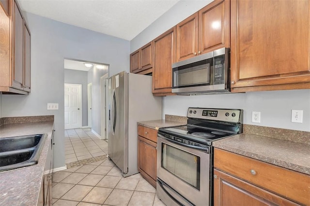 kitchen featuring light tile patterned floors, a sink, brown cabinets, dark countertops, and stainless steel appliances