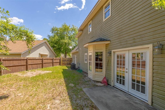 view of yard with central AC unit, french doors, and a fenced backyard