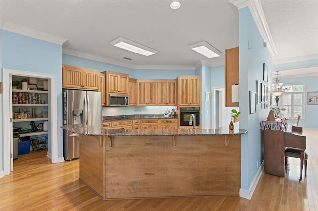 kitchen with appliances with stainless steel finishes, a breakfast bar area, dark stone countertops, crown molding, and light wood-style floors