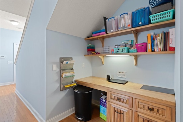 office area with vaulted ceiling, light wood finished floors, built in study area, and baseboards