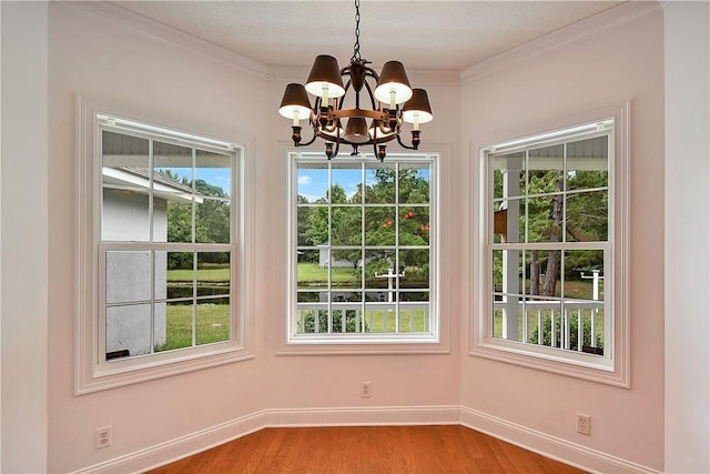 unfurnished dining area with a chandelier, hardwood / wood-style floors, a textured ceiling, and crown molding