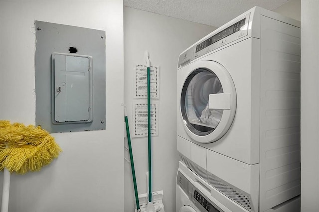 laundry area with a textured ceiling, electric panel, and stacked washing maching and dryer