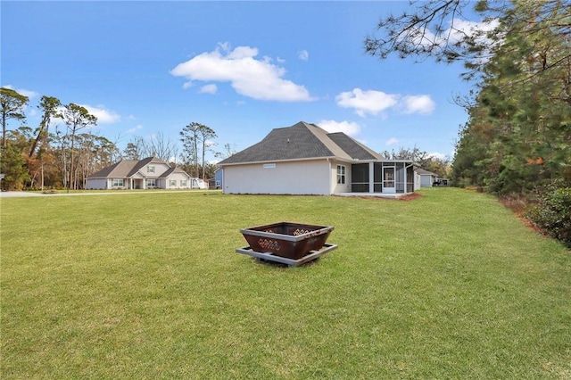 back of property featuring a sunroom, a yard, and a fire pit