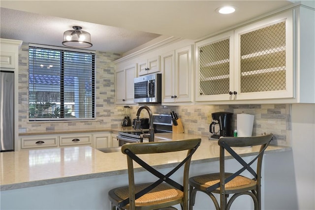 kitchen with a kitchen bar, decorative backsplash, white cabinets, and stainless steel appliances