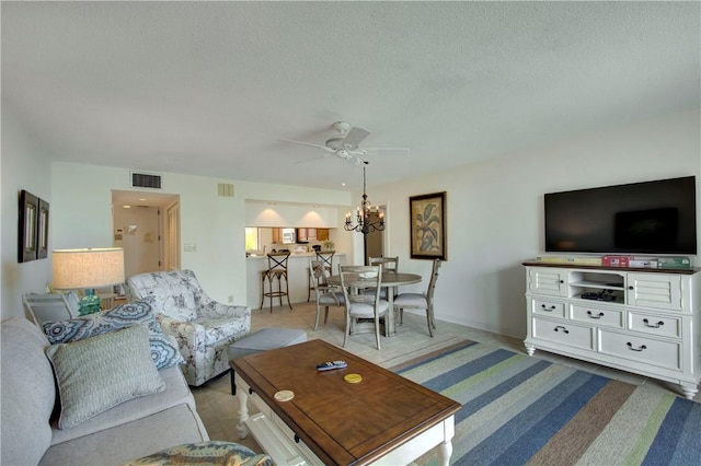 living room featuring ceiling fan with notable chandelier and a textured ceiling