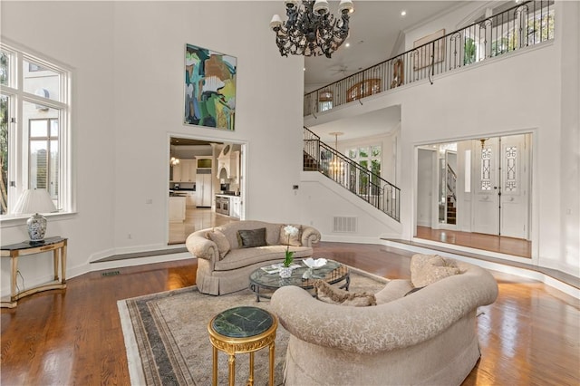 living room featuring an inviting chandelier, a towering ceiling, a healthy amount of sunlight, and hardwood / wood-style flooring