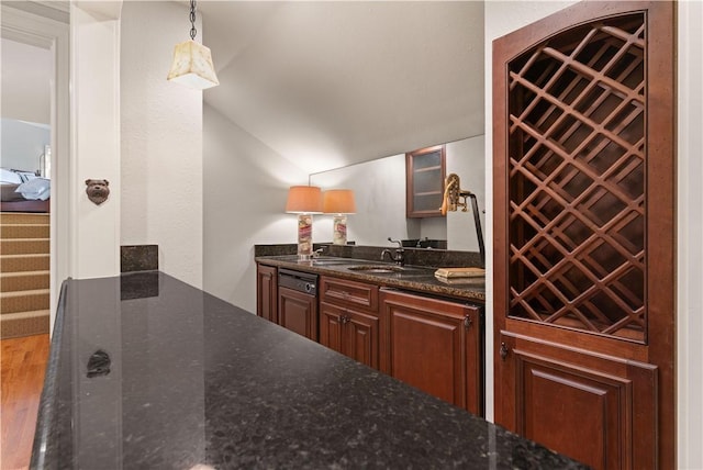 kitchen featuring dark stone counters, sink, wood-type flooring, hanging light fixtures, and lofted ceiling