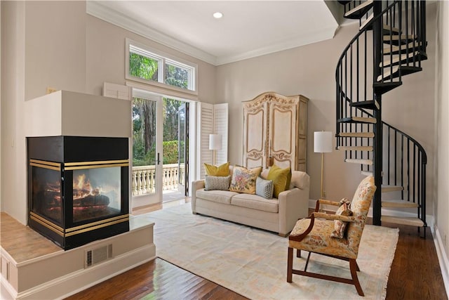 living room featuring a multi sided fireplace, a high ceiling, hardwood / wood-style flooring, and ornamental molding