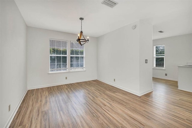 spare room with plenty of natural light, a notable chandelier, and light wood-type flooring