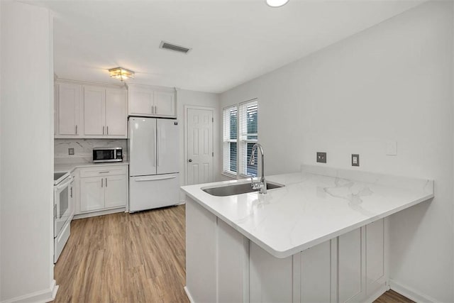 kitchen with kitchen peninsula, white appliances, sink, light hardwood / wood-style flooring, and white cabinets