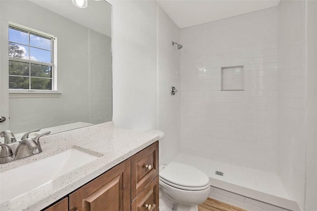 bathroom featuring tiled shower, vanity, wood-type flooring, and toilet