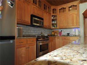 105 Lonnie Johnson Rd, Hazlehurst, GA 31539 - kitchen featuring appliances with stainless steel finishes, tasteful backsplash, glass insert cabinets, light stone countertops, and brown cabinets
