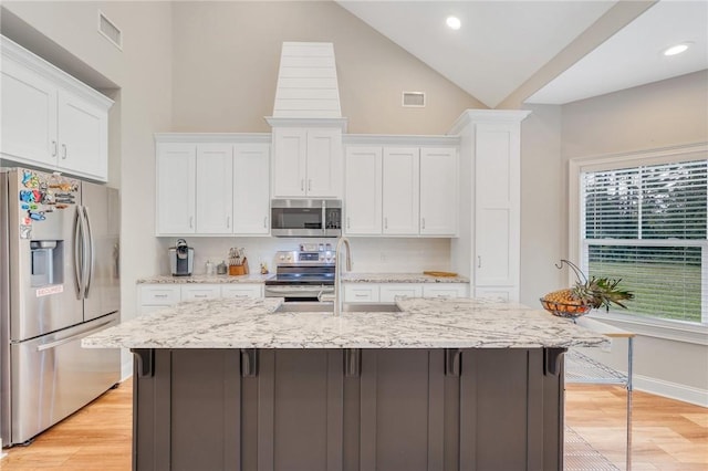 kitchen featuring light hardwood / wood-style floors, white cabinetry, stainless steel appliances, and a kitchen island with sink