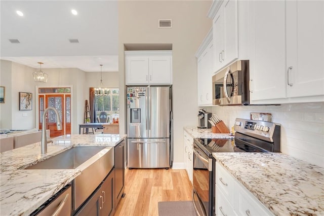 kitchen with stainless steel appliances, pendant lighting, an inviting chandelier, light hardwood / wood-style floors, and white cabinetry