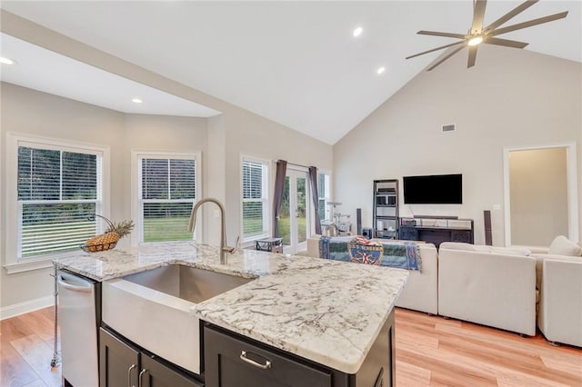 kitchen featuring light stone counters, sink, a center island with sink, high vaulted ceiling, and light hardwood / wood-style floors