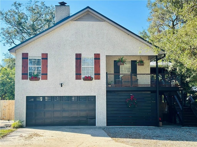 view of front of house featuring stairway, stucco siding, a chimney, a garage, and driveway