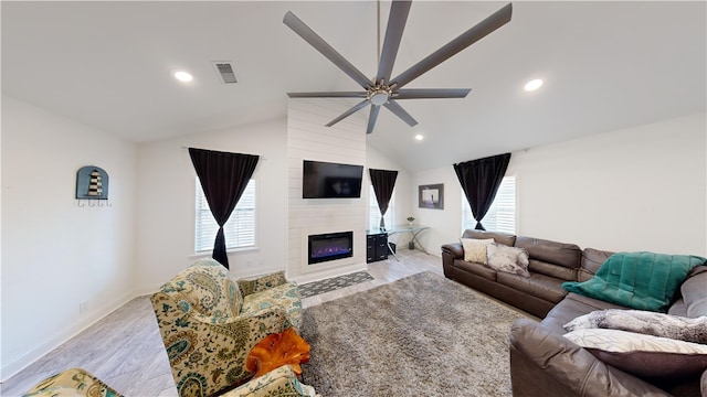 living room with vaulted ceiling, a large fireplace, ceiling fan, and light wood-type flooring