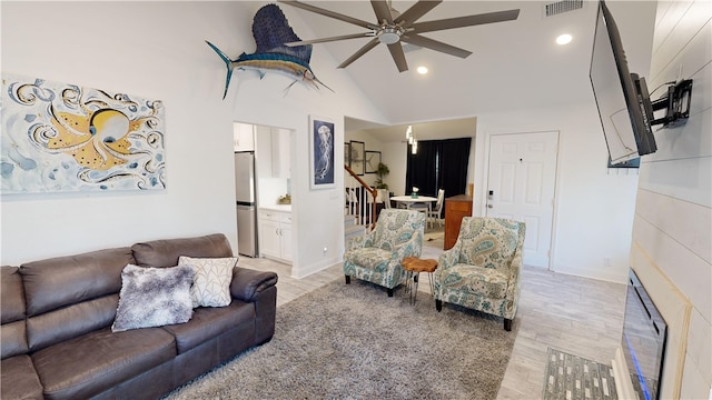 living area featuring visible vents, high vaulted ceiling, light wood-style flooring, ceiling fan, and stairs