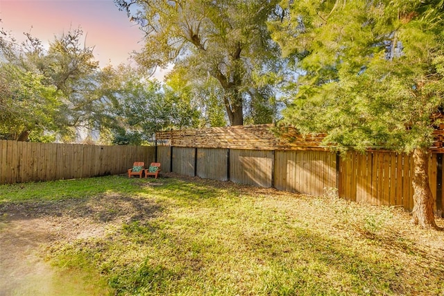 yard at dusk featuring a fenced backyard