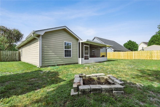 back of property featuring a sunroom, a yard, a fenced backyard, and an outdoor fire pit