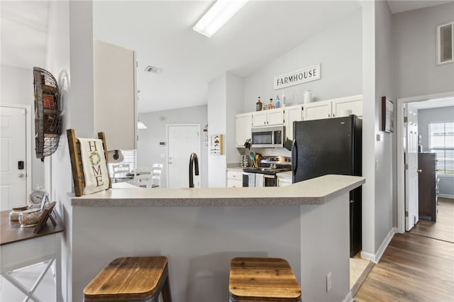 kitchen featuring a sink, light wood-type flooring, a peninsula, appliances with stainless steel finishes, and lofted ceiling