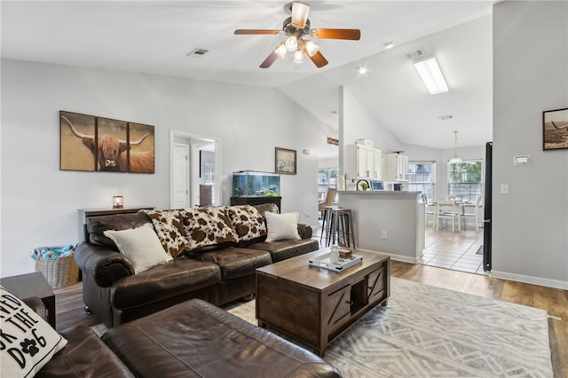 living area with visible vents, baseboards, light wood-type flooring, a ceiling fan, and high vaulted ceiling