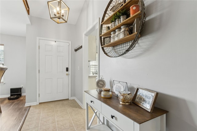 foyer featuring baseboards, light tile patterned floors, and an inviting chandelier