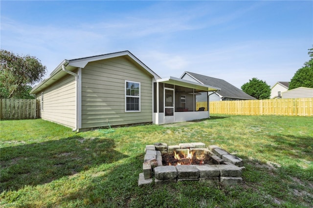 back of house with an outdoor fire pit, a fenced backyard, a yard, and a sunroom