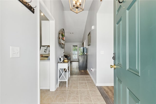 foyer entrance with baseboards, light tile patterned floors, an inviting chandelier, and vaulted ceiling