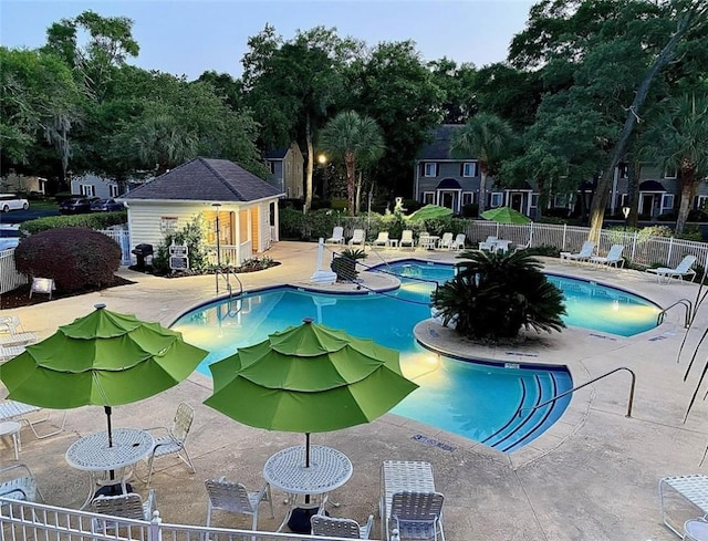 community pool with a patio, fence, and an outbuilding