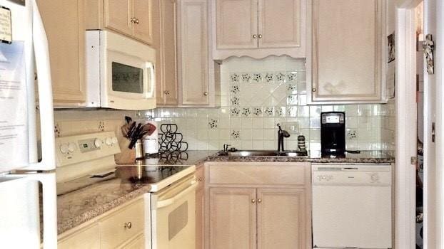 kitchen with a sink, tasteful backsplash, white appliances, and dark stone countertops