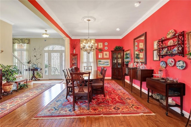 dining room with ornate columns, ornamental molding, wood-type flooring, and a notable chandelier