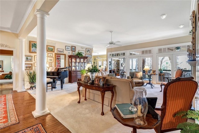 living area with french doors, crown molding, a ceiling fan, light wood-style floors, and ornate columns