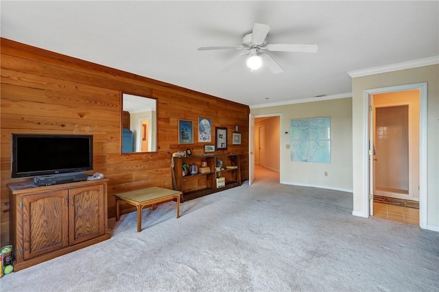 living area with ceiling fan, light colored carpet, wood walls, baseboards, and crown molding