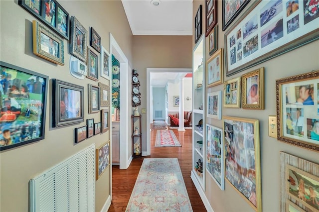 hallway featuring dark wood-type flooring, visible vents, crown molding, and baseboards