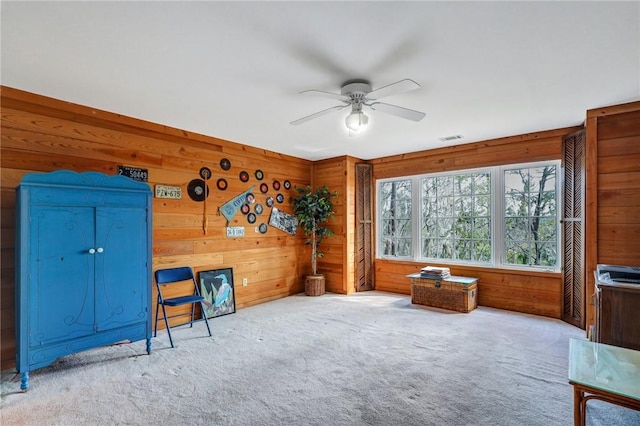 living area featuring a ceiling fan, visible vents, wood walls, and carpet flooring