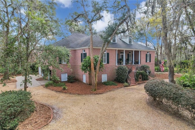 view of side of property featuring a porch, brick siding, driveway, crawl space, and stairway