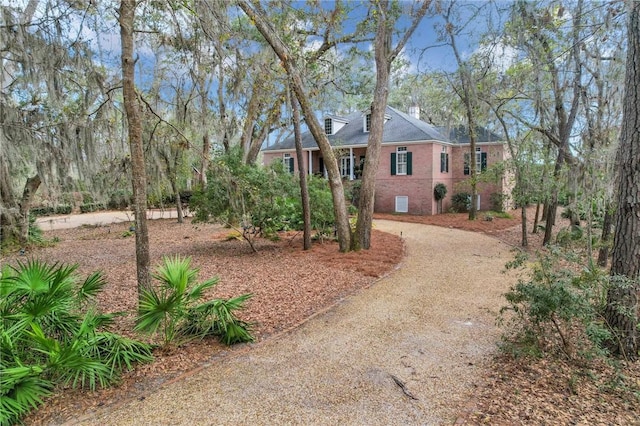 view of front of property with brick siding, driveway, and a chimney