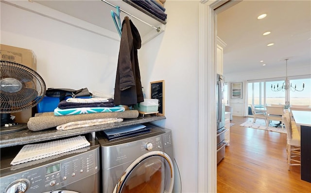 clothes washing area featuring a chandelier, light hardwood / wood-style floors, and washing machine and clothes dryer