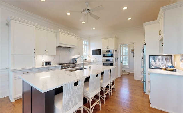 kitchen with light stone countertops, stainless steel appliances, light hardwood / wood-style floors, white cabinets, and ornamental molding