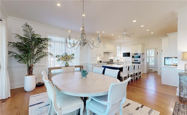 dining space featuring sink, light hardwood / wood-style flooring, ceiling fan with notable chandelier, and ornamental molding