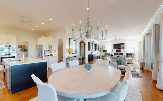 dining area featuring ceiling fan with notable chandelier, light hardwood / wood-style floors, ornamental molding, and sink