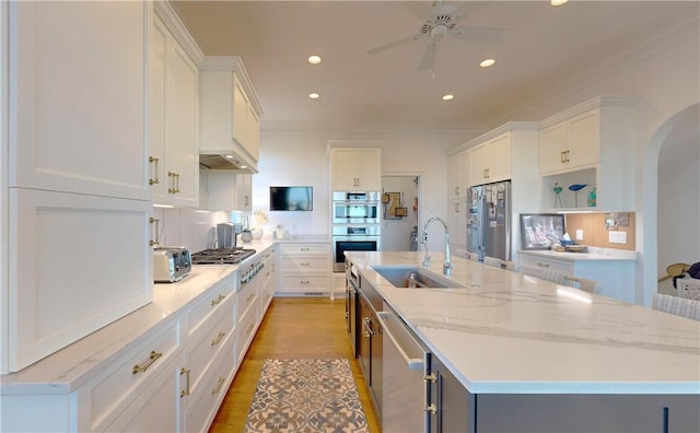 kitchen with white cabinetry, sink, stainless steel appliances, an island with sink, and light wood-type flooring