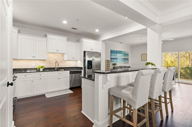 kitchen with visible vents, appliances with stainless steel finishes, a kitchen breakfast bar, dark wood-style floors, and a sink