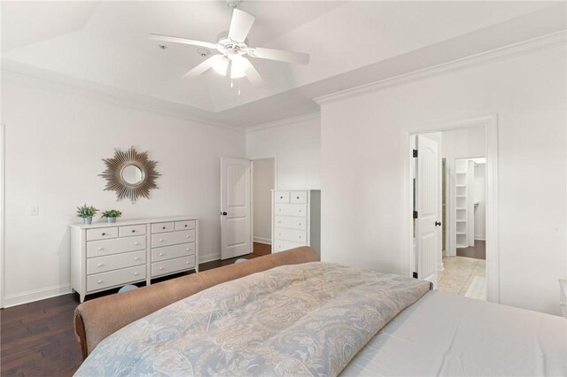 bedroom featuring a raised ceiling, ornamental molding, a ceiling fan, wood finished floors, and baseboards