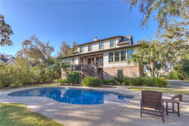 back of house with brick siding, stairs, a chimney, an outdoor pool, and a patio